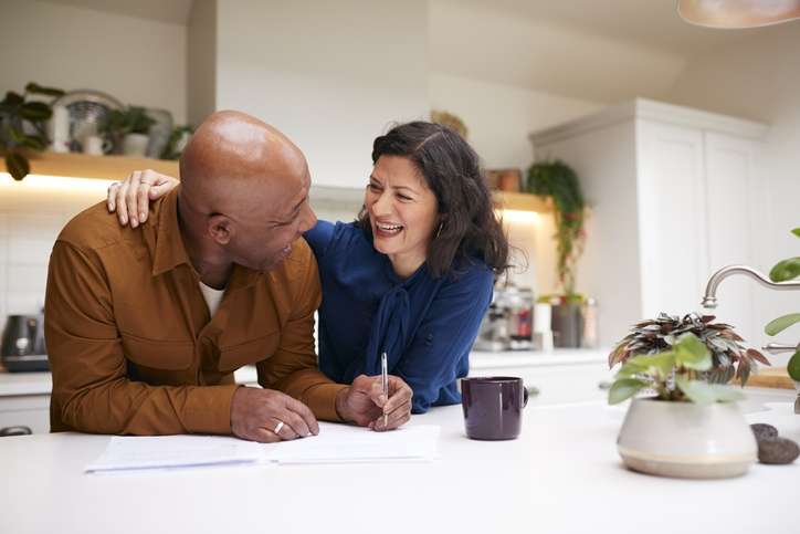 Mature Couple Reviewing And Signing Domestic Finances And Investment downsizing home In Kitchen At Home