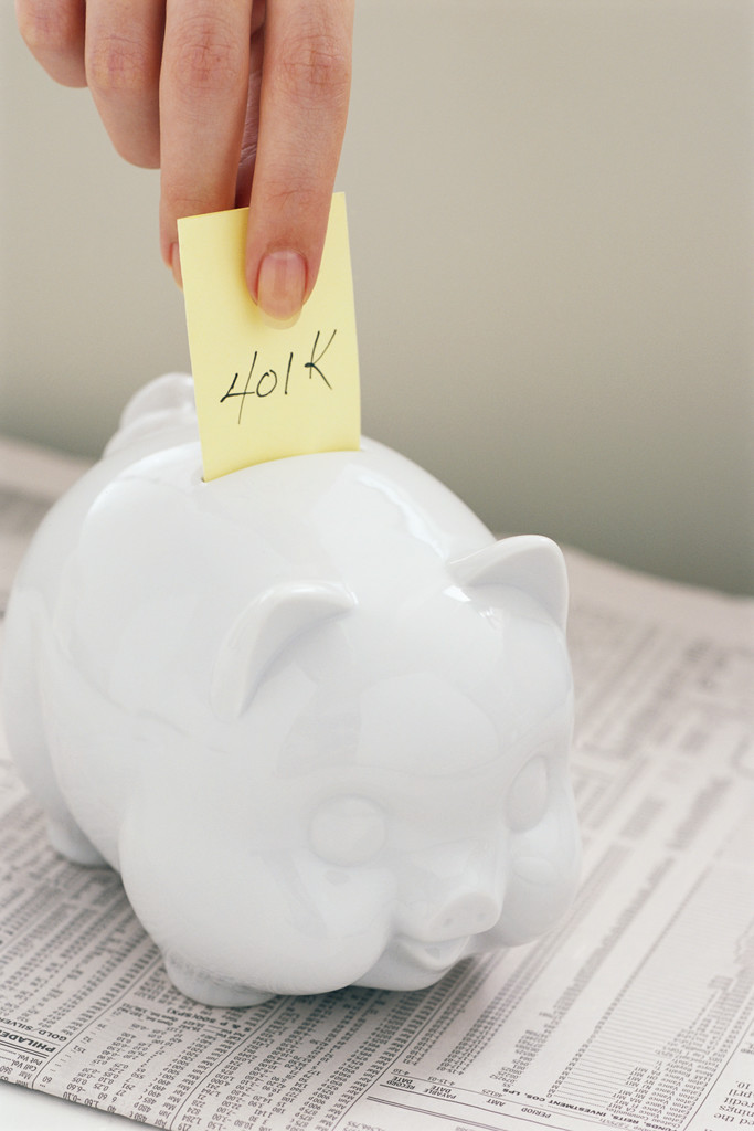 Hand Putting Note Reading "401K" into Piggy Bank