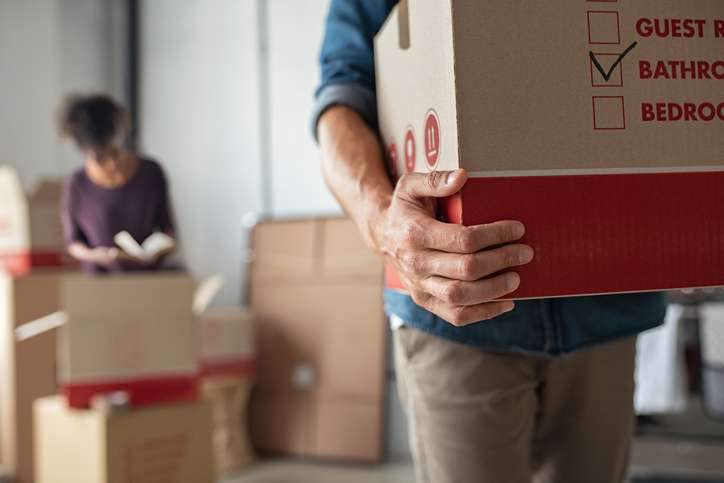 Closeup of man hand holding cardboard at new home. Young man unpacking boxes in new apartment. Man hand carrying carton box while relocating with his girlfriend.