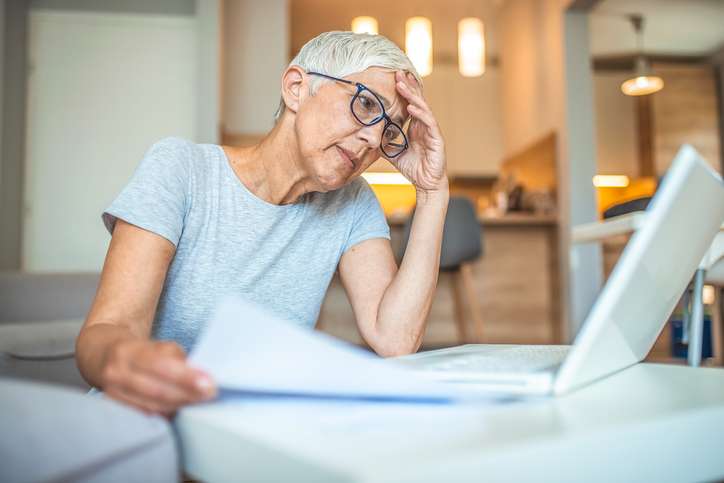 Woman preparing home budget, using laptop and calculator. Woman going through bills, looking worried. Shot of a senior woman using a laptop and calculator while working from home